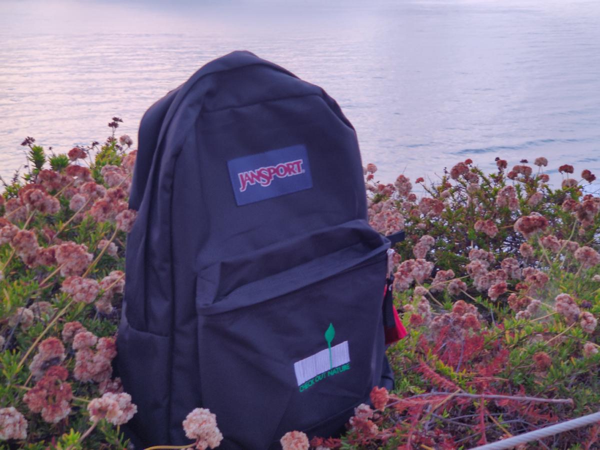 Image of the Nature Explore Backpack and a bed of flowers