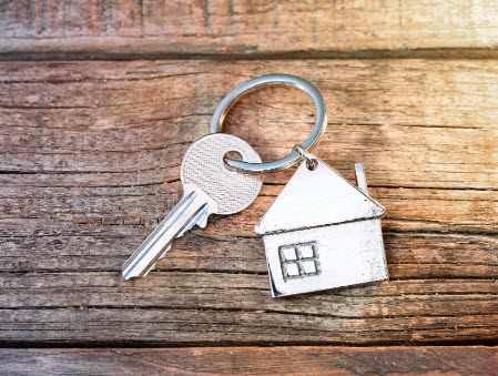 picture of a silver house keychain with one key attached and a background made of destressed wood